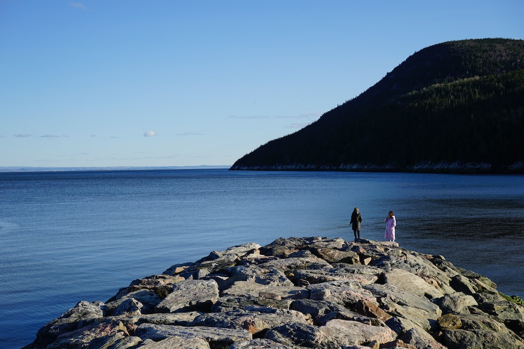 2 person standing on rock formation near body of water during daytime