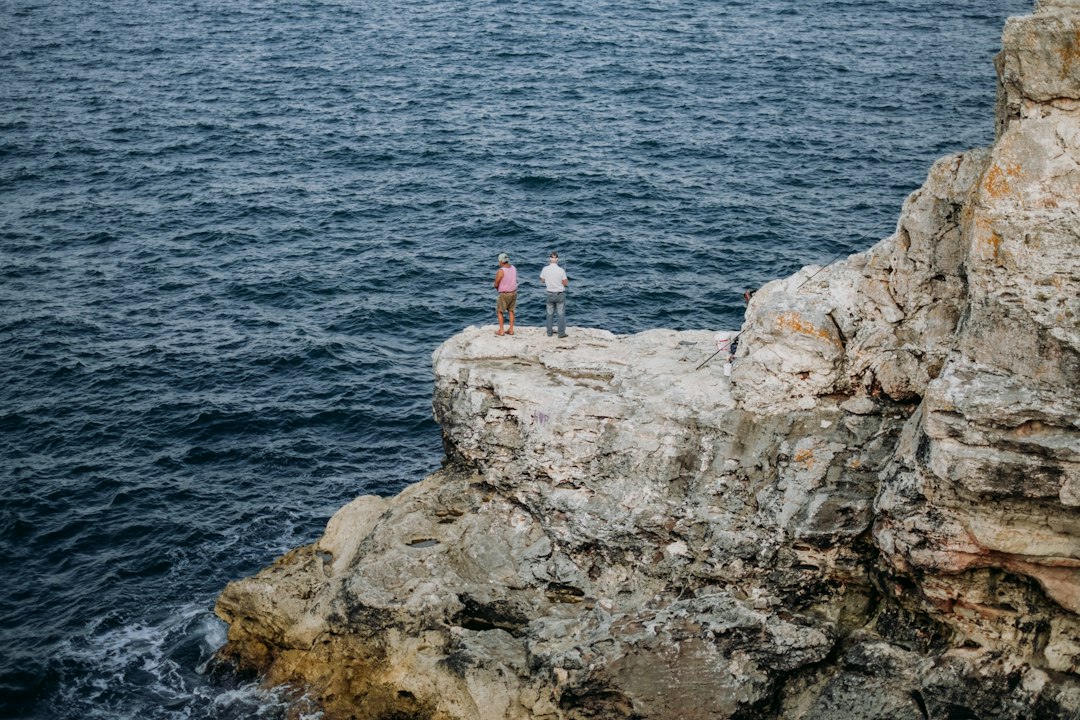 a couple of people standing on a rock by the water