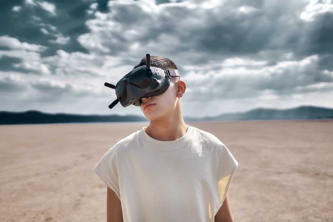 man in white crew neck t-shirt wearing black sunglasses standing on brown sand during daytime