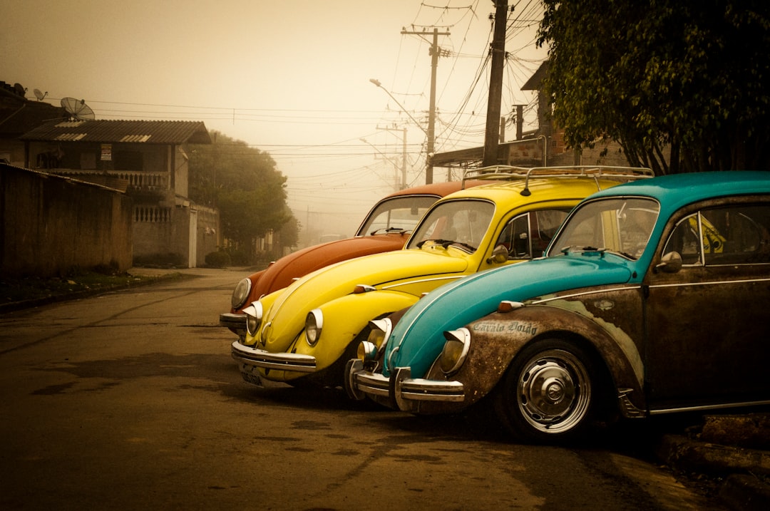 three assorted-color Volkswagen Beetle coups parked near houses