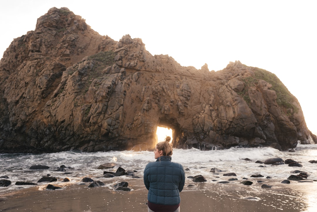 man in blue and black jacket sitting on rock formation in front of sea during daytime