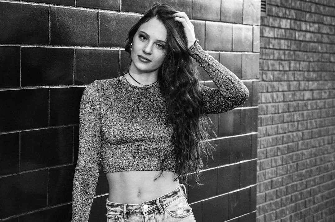 woman in gray sweater standing beside brick wall